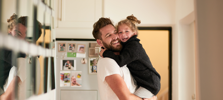 Father holding his smiling young child in a kitchen